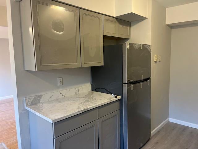 kitchen featuring stainless steel fridge, light stone counters, gray cabinetry, and hardwood / wood-style floors