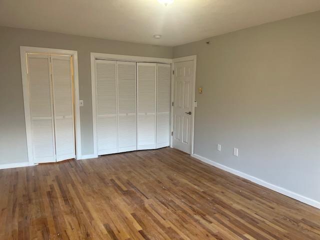 unfurnished bedroom featuring wood-type flooring and multiple closets