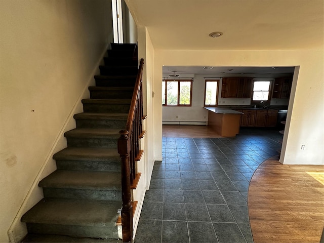 staircase with tile patterned flooring, ceiling fan, a baseboard heating unit, and sink