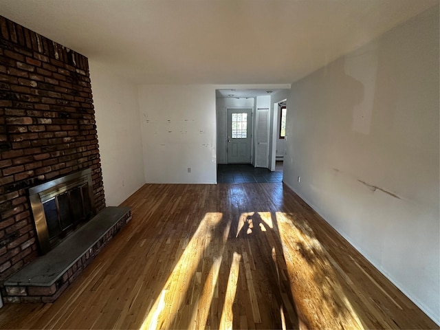 unfurnished living room featuring a brick fireplace and dark wood-type flooring