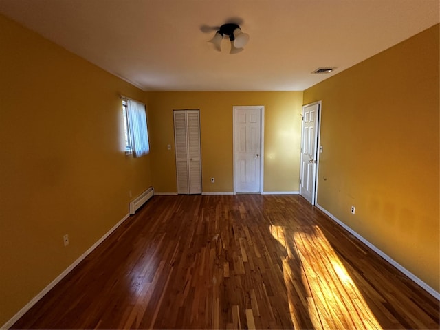 unfurnished bedroom with dark hardwood / wood-style flooring and baseboard heating