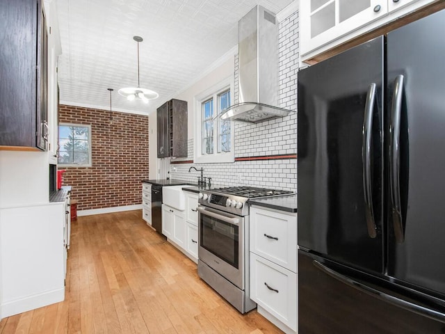 kitchen featuring white cabinetry, wall chimney exhaust hood, black fridge, brick wall, and high end stove