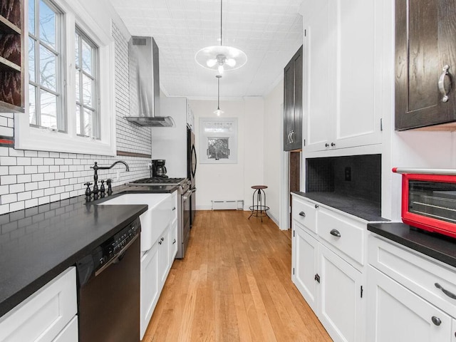 kitchen featuring pendant lighting, wall chimney range hood, black dishwasher, a baseboard radiator, and white cabinetry