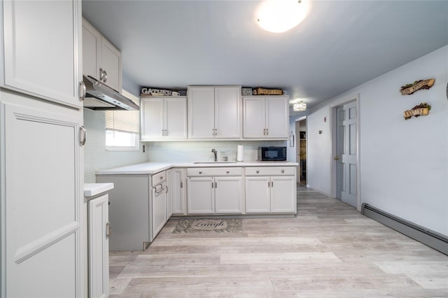 kitchen with backsplash, white cabinets, sink, light wood-type flooring, and baseboard heating