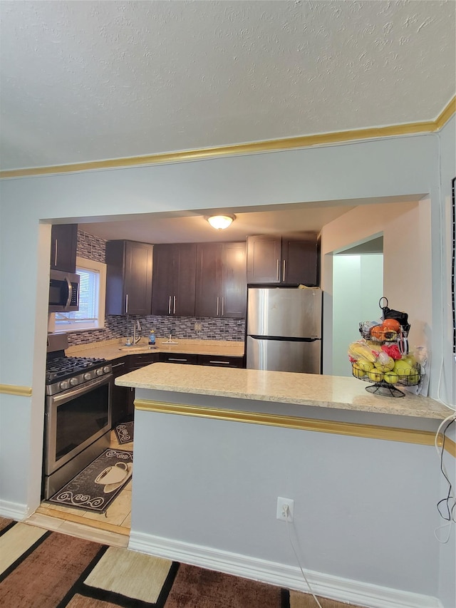 kitchen featuring kitchen peninsula, decorative backsplash, dark brown cabinetry, and stainless steel appliances