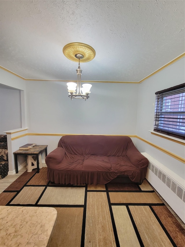 living room featuring radiator heating unit, ornamental molding, a textured ceiling, and a notable chandelier