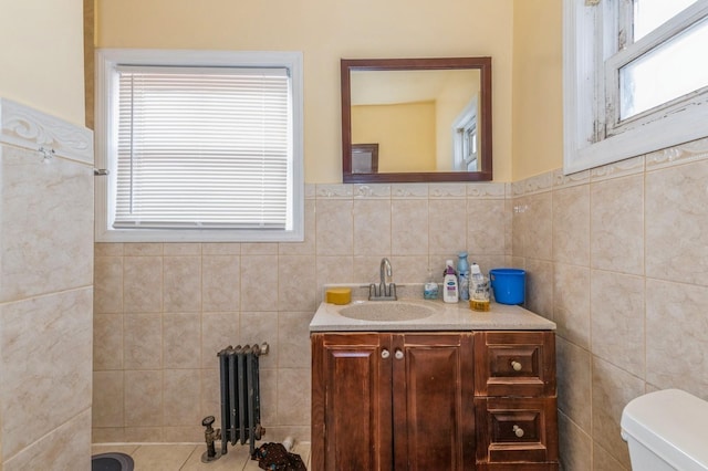 bathroom featuring vanity, toilet, radiator heating unit, and tile walls