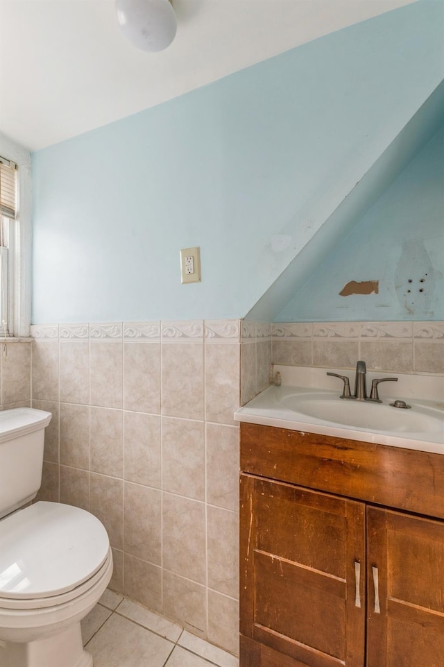 bathroom with vanity, lofted ceiling, tile patterned flooring, toilet, and tile walls