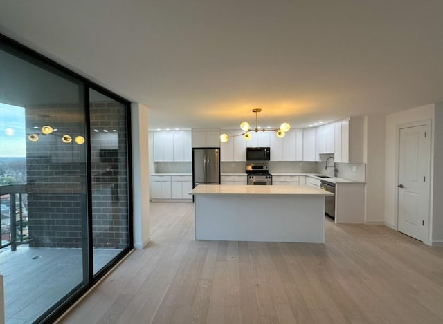 kitchen with appliances with stainless steel finishes, light wood-type flooring, expansive windows, decorative light fixtures, and white cabinetry