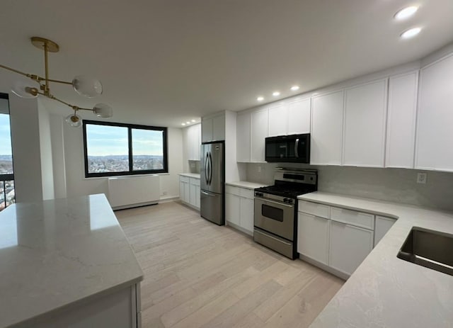 kitchen with light stone countertops, light wood-type flooring, stainless steel appliances, sink, and white cabinetry