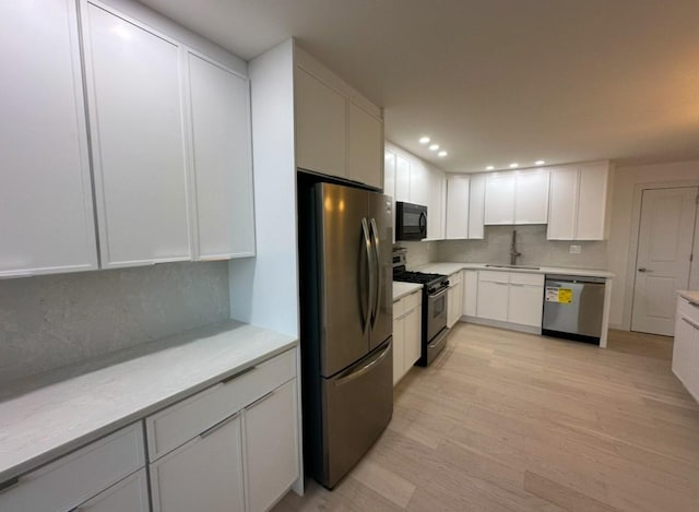 kitchen featuring white cabinetry, sink, stainless steel appliances, decorative backsplash, and light wood-type flooring