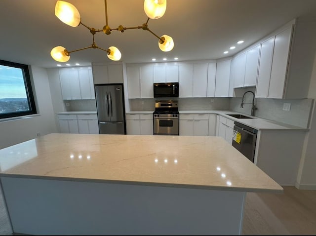 kitchen with appliances with stainless steel finishes, light stone counters, sink, white cabinets, and hanging light fixtures