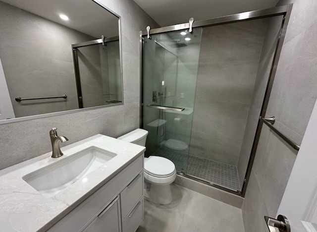 bathroom with vanity, toilet, tile walls, and a shower with shower door