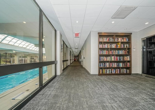 corridor with built in shelves, a paneled ceiling, and dark carpet