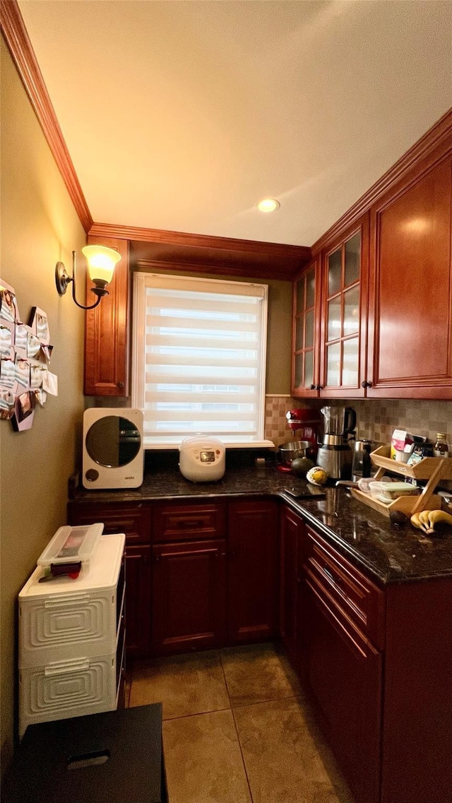 kitchen with decorative backsplash, dark tile patterned flooring, crown molding, and dark stone countertops