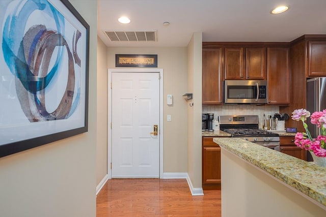 kitchen with light stone counters, tasteful backsplash, stainless steel appliances, and light wood-type flooring