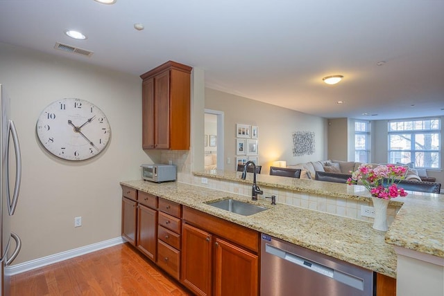 kitchen featuring sink, stainless steel appliances, light stone countertops, light hardwood / wood-style floors, and backsplash