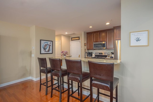 kitchen with appliances with stainless steel finishes, a breakfast bar, tasteful backsplash, hardwood / wood-style flooring, and light stone counters