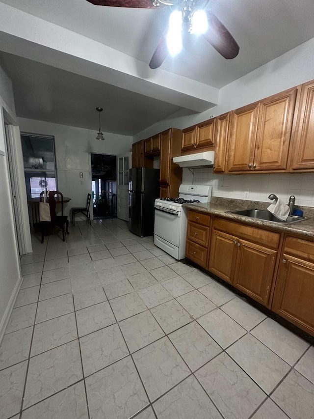 kitchen with black refrigerator, backsplash, ceiling fan, sink, and white range with gas stovetop