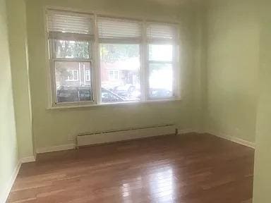 unfurnished room featuring a baseboard heating unit and hardwood / wood-style floors