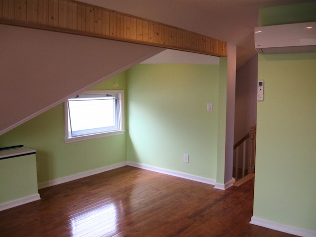 bonus room with dark hardwood / wood-style flooring and a wall unit AC