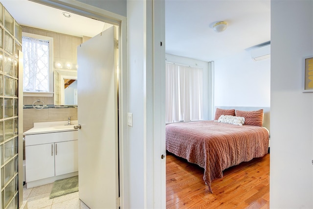 bedroom featuring a wall unit AC, light hardwood / wood-style flooring, and sink