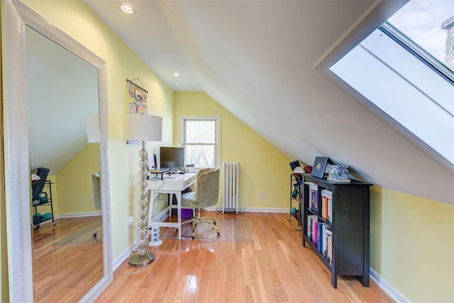 office space featuring lofted ceiling with skylight, wood-type flooring, and radiator heating unit