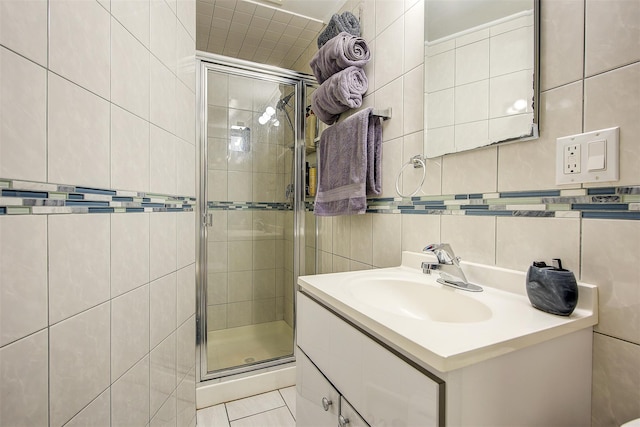 bathroom with tile patterned floors, a shower with door, vanity, tasteful backsplash, and tile walls