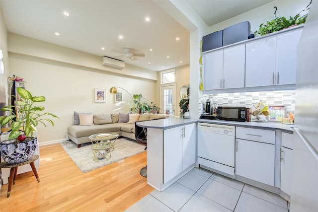 kitchen with white cabinets, a wall unit AC, kitchen peninsula, and dishwasher