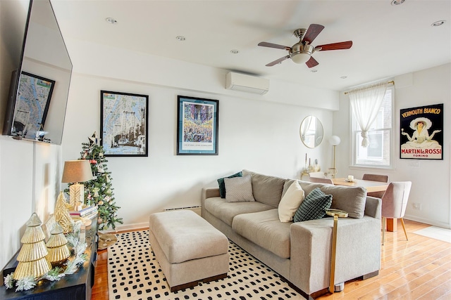 living room featuring baseboard heating, ceiling fan, a wall unit AC, and light wood-type flooring