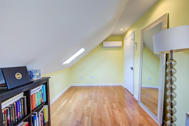 additional living space with vaulted ceiling with skylight, hardwood / wood-style floors, and a wall unit AC