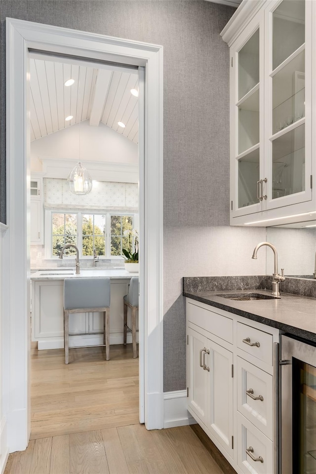 bar featuring sink, white cabinetry, light wood-type flooring, pendant lighting, and beverage cooler