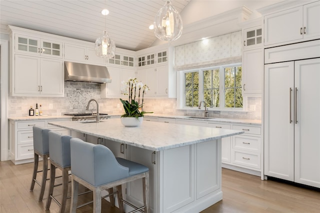 kitchen featuring pendant lighting, range hood, sink, white cabinets, and a kitchen island with sink