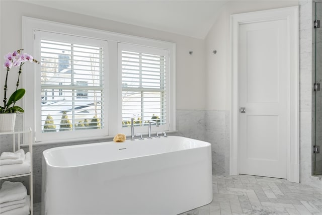 bathroom with vaulted ceiling, a wealth of natural light, a bathtub, and tile walls