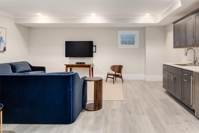 living room with crown molding, sink, light hardwood / wood-style floors, and a tray ceiling