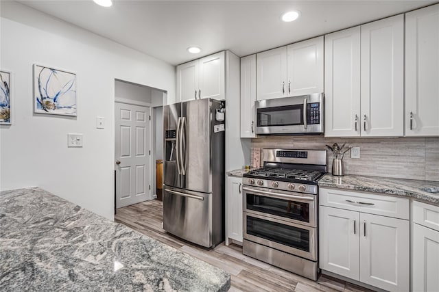 kitchen featuring white cabinets, stainless steel appliances, and light stone counters