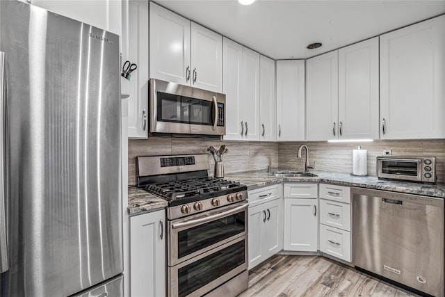 kitchen featuring stainless steel appliances, sink, white cabinets, light stone counters, and light hardwood / wood-style floors