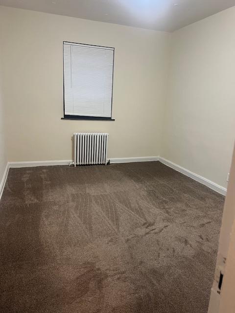 unfurnished room featuring radiator and dark colored carpet