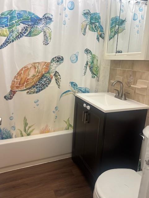 full bathroom featuring toilet, decorative backsplash, shower / tub combo with curtain, vanity, and hardwood / wood-style flooring