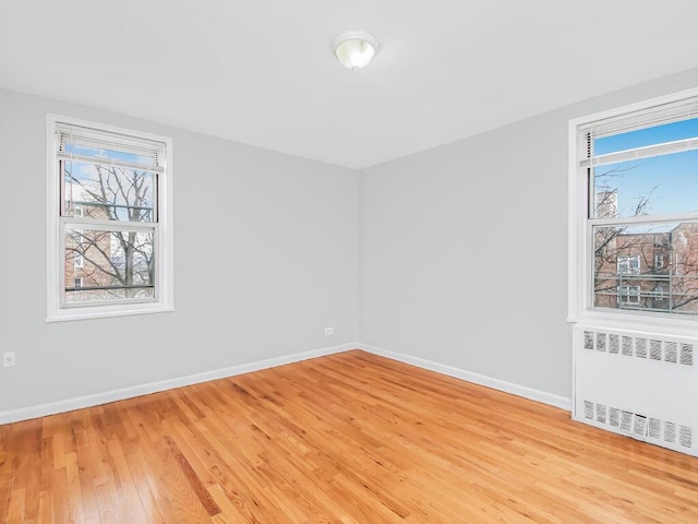 spare room with a healthy amount of sunlight, radiator heating unit, and light wood-type flooring