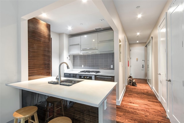 kitchen with a kitchen breakfast bar, backsplash, stainless steel gas cooktop, sink, and hardwood / wood-style floors