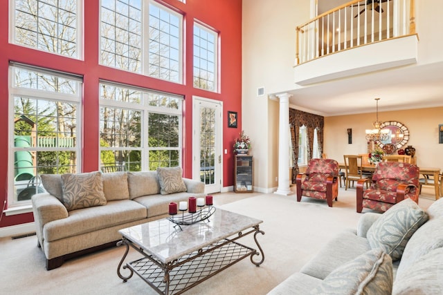 living room with light carpet, a towering ceiling, decorative columns, crown molding, and an inviting chandelier