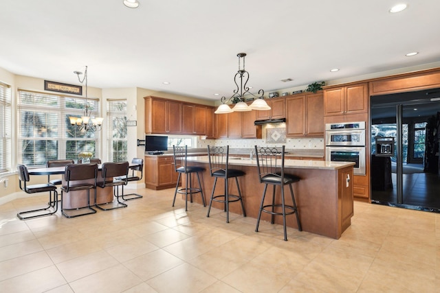 kitchen featuring stainless steel double oven, an inviting chandelier, decorative light fixtures, black refrigerator, and a center island with sink