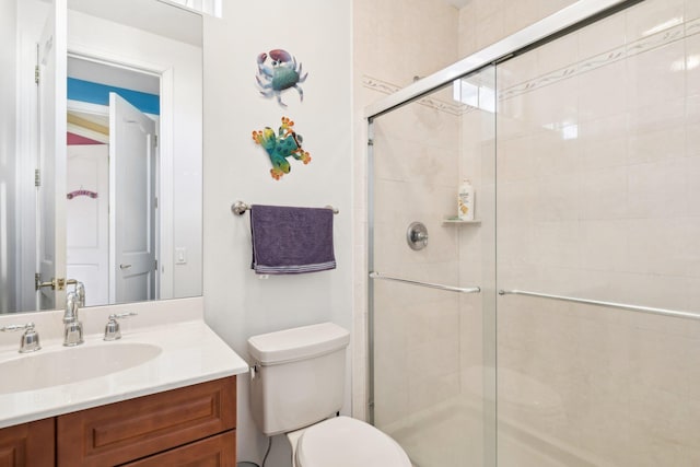 bathroom featuring a shower with door, vanity, and toilet