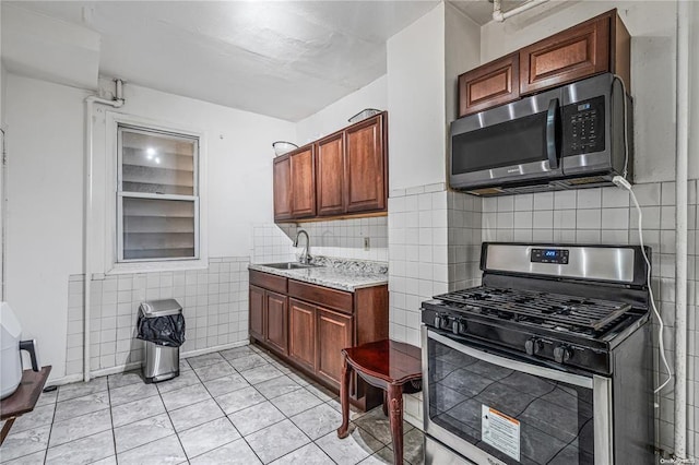 kitchen with sink, light tile patterned floors, tile walls, and appliances with stainless steel finishes