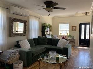 living room with a wall mounted air conditioner, wood-type flooring, ceiling fan, crown molding, and french doors