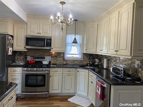 kitchen featuring wood finished floors, appliances with stainless steel finishes, decorative backsplash, dark countertops, and decorative light fixtures