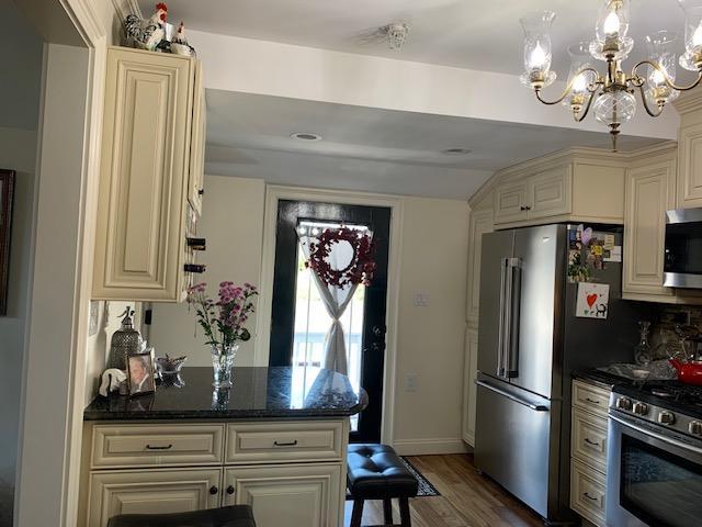 kitchen with appliances with stainless steel finishes, cream cabinets, dark stone countertops, and dark wood finished floors