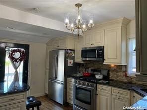 kitchen with wood finished floors, appliances with stainless steel finishes, tasteful backsplash, dark countertops, and an inviting chandelier