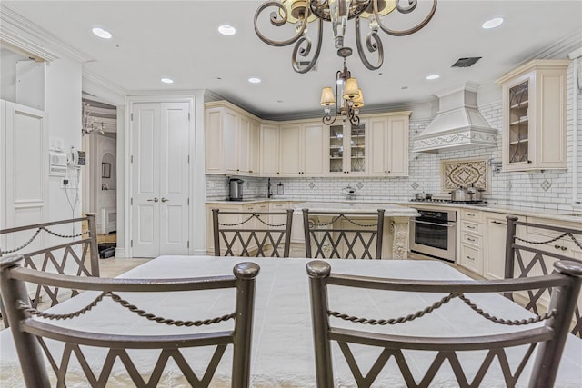 kitchen with stainless steel appliances, premium range hood, cream cabinets, decorative backsplash, and a breakfast bar